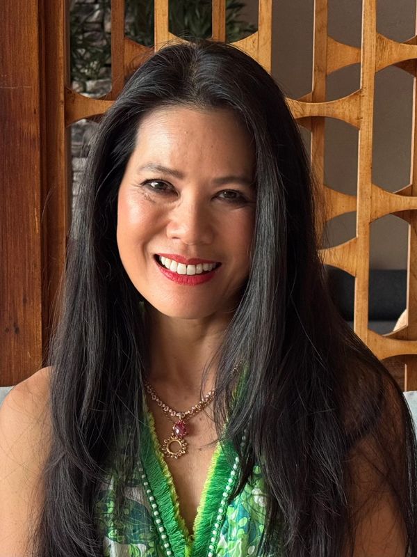 A smiling woman with long black hair wearing a green patterned top and a necklace.