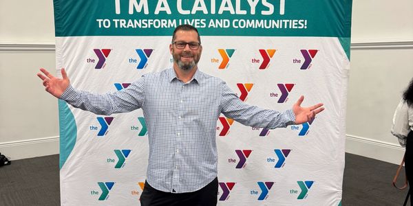 Man with open arms in front of a YMCA banner.