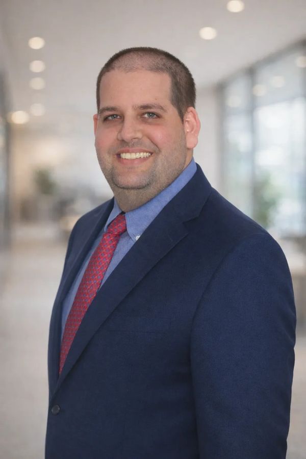 Smiling man in a navy suit and red tie in a professional setting.