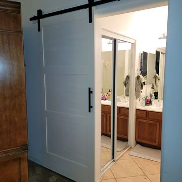 Modern white sliding barn door leading to a bathroom with wooden cabinets.