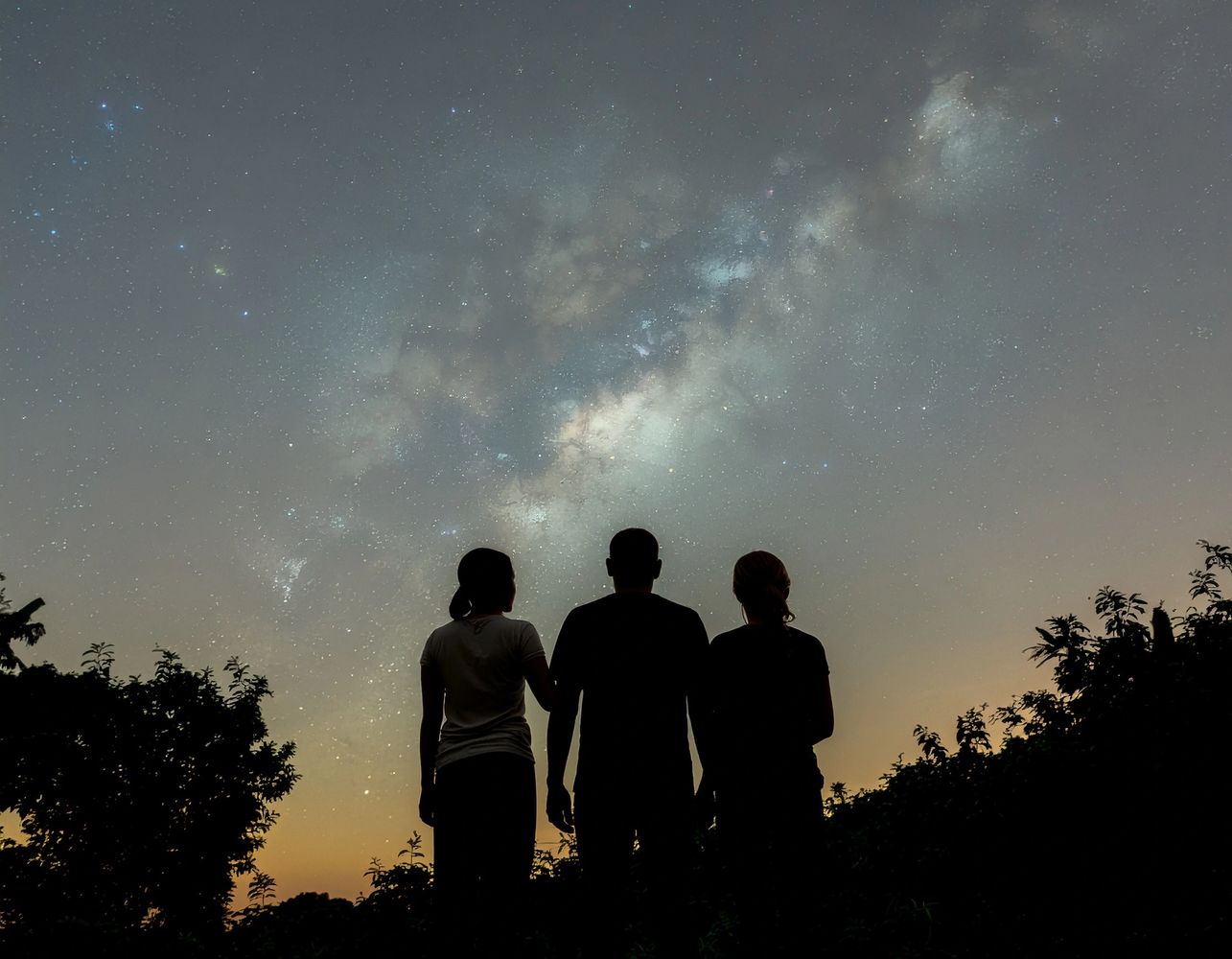 Three people silhouette stargazing under a vibrant Milky Way at dusk.