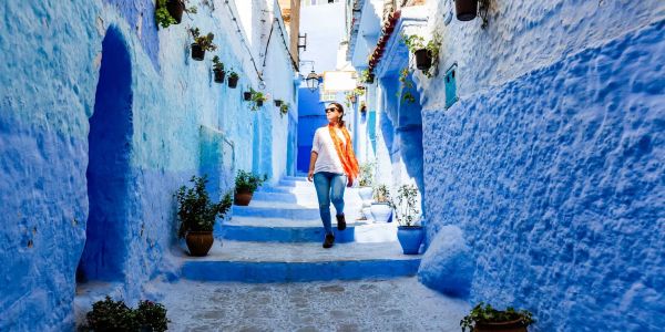 A woman walking through a vibrant blue-painted street adorned with potted plants.
