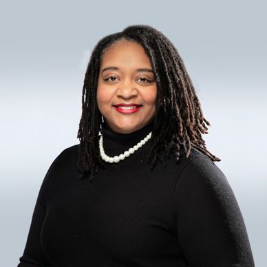 Professional woman with dreadlocks, wearing a black top and pearl necklace, smiling confidently.
