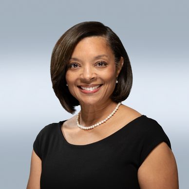Professional woman with short hair wearing a black dress and pearl necklace.