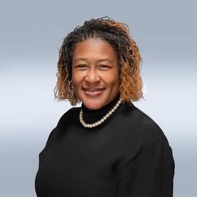 Smiling woman with curly hair wearing a black top and pearl necklace.