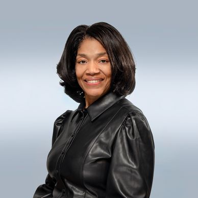 Confident woman smiling, wearing a black leather shirt against a light blue background.