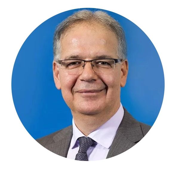 Professional headshot of a middle-aged man in a suit and glasses against a blue background.