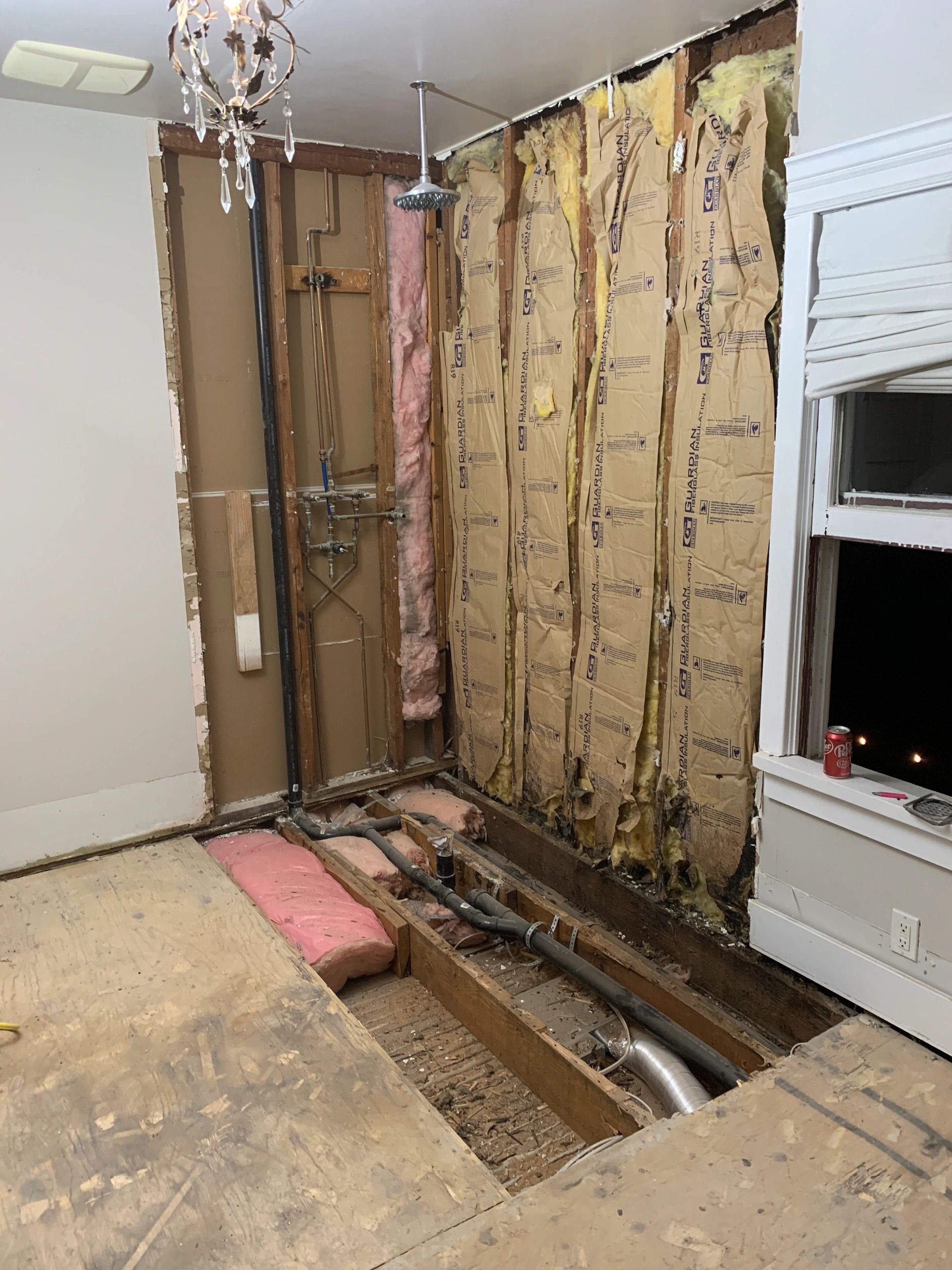 Bathroom under renovation with exposed pipes and insulation.