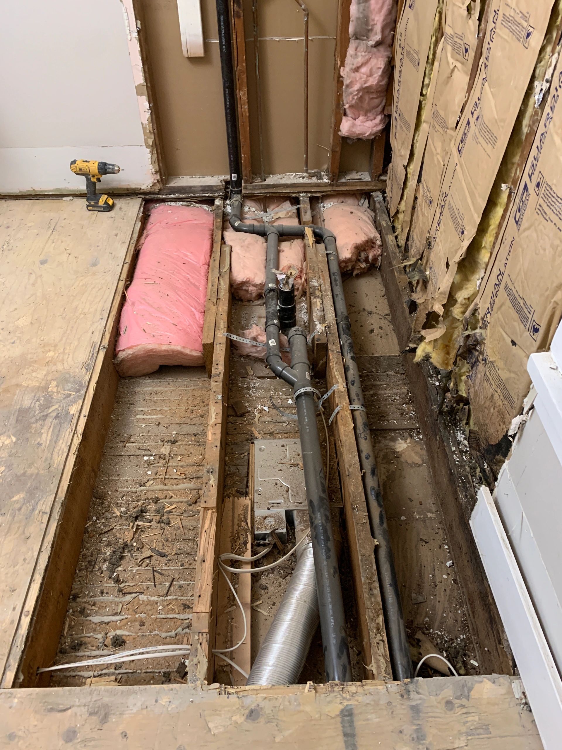 Floor removed showing pipes and insulation inside a wall.