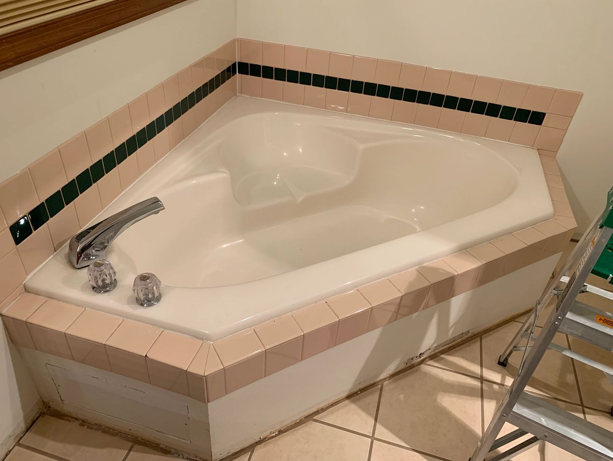 Corner bathtub with pink and black tiles in a bathroom under renovation.