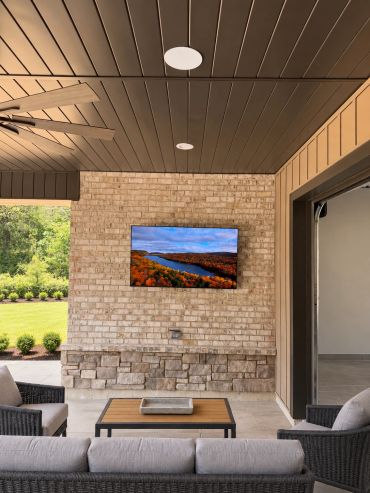 Custom covered-patio entertainment area featuring a professionally mounted outdoor TV, in-ceiling sp
