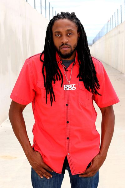 Man with dreadlocks wearing a bright red shirt and a 'BUT GOD' necklace.
