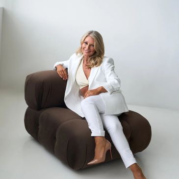 Woman in white outfit sitting on a brown modern couch.