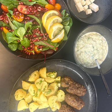 A meal with salad, potatoes, meat, cheese, and creamy cucumber sauce.