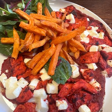 Plate with grilled chicken, cheese, sweet potato fries, and leafy greens.