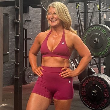 Smiling woman in pink workout attire stands confidently in a gym.