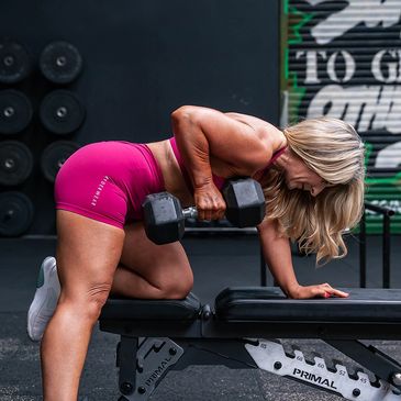 Woman lifting dumbbell with bench support in gym workout.
