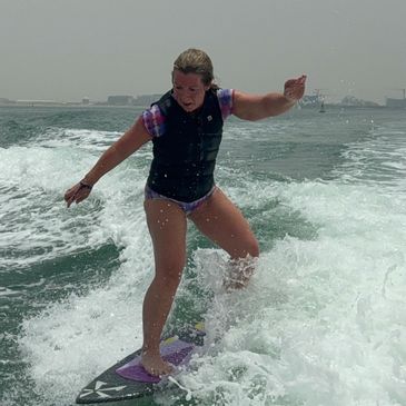 A woman wakesurfs on ocean waves near a boat.