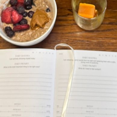 A breakfast setup with flowers, oatmeal, candle, vitamins, and an open planner on a wooden table.