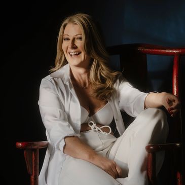 Woman in white outfit smiling while sitting on a red wooden chair.