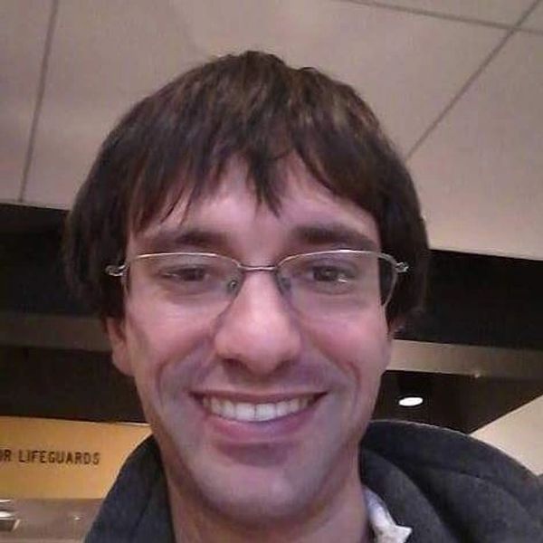 Young man with glasses smiling indoors.