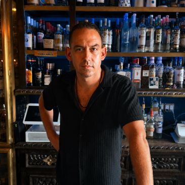 Confident bartender standing behind a bar with various liquor bottles.