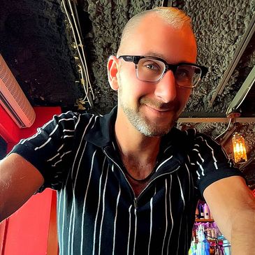Smiling man wearing glasses and a striped shirt in a cozy bar setting.