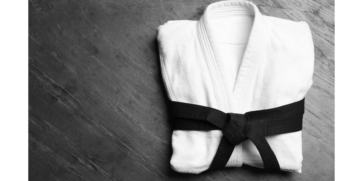 A white martial arts uniform sits folded on a table with a black belt wrapped around it.
