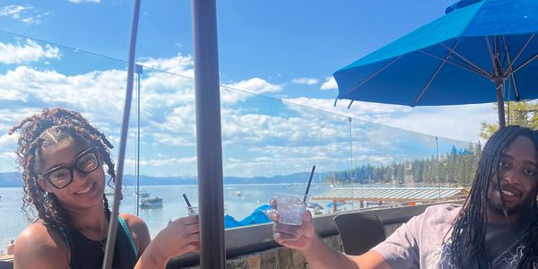Two women enjoying drinks outdoors under a bright blue sky with umbrellas.