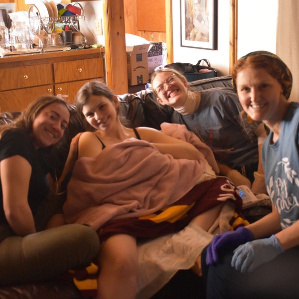 Four women smiling together on a couch.