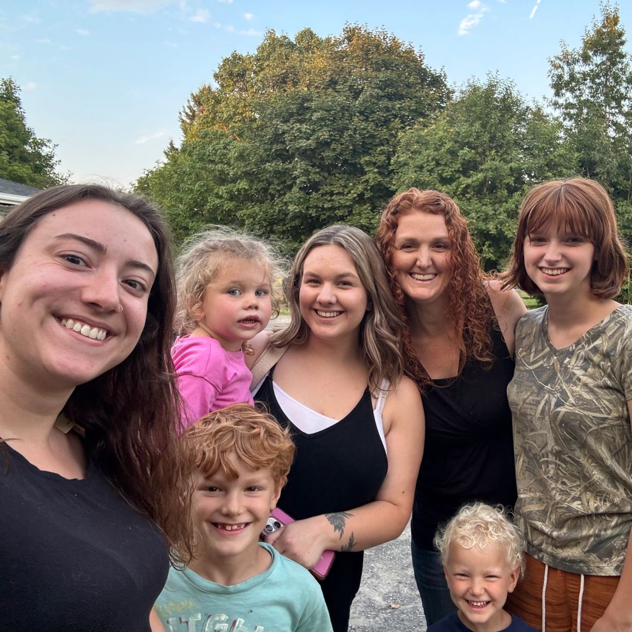 Group selfie of smiling women and children outdoors.