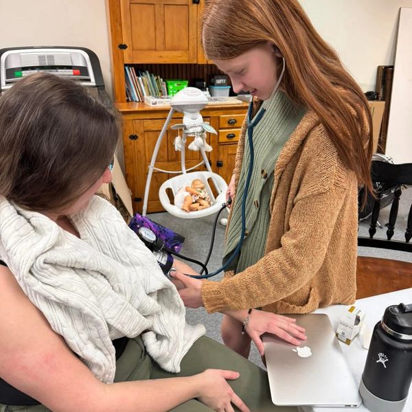 Girl using a stethoscope to take another person's blood pressure.