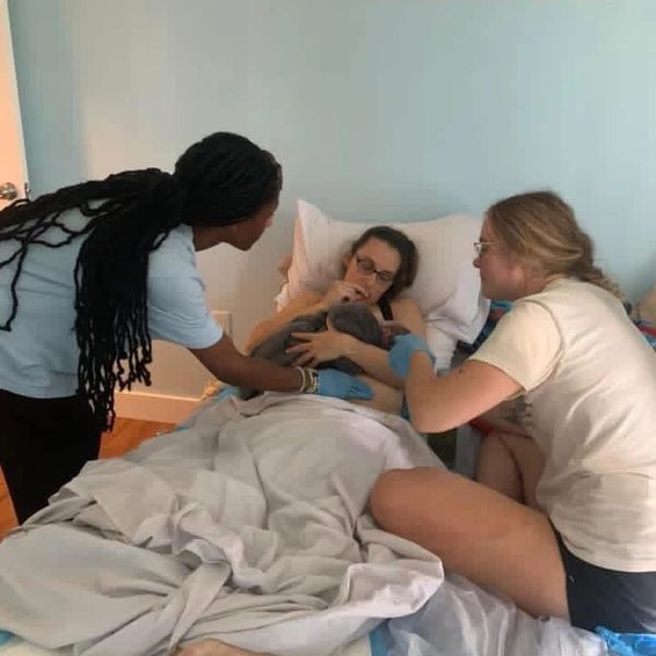 Two women helping a person in bed with a small animal.