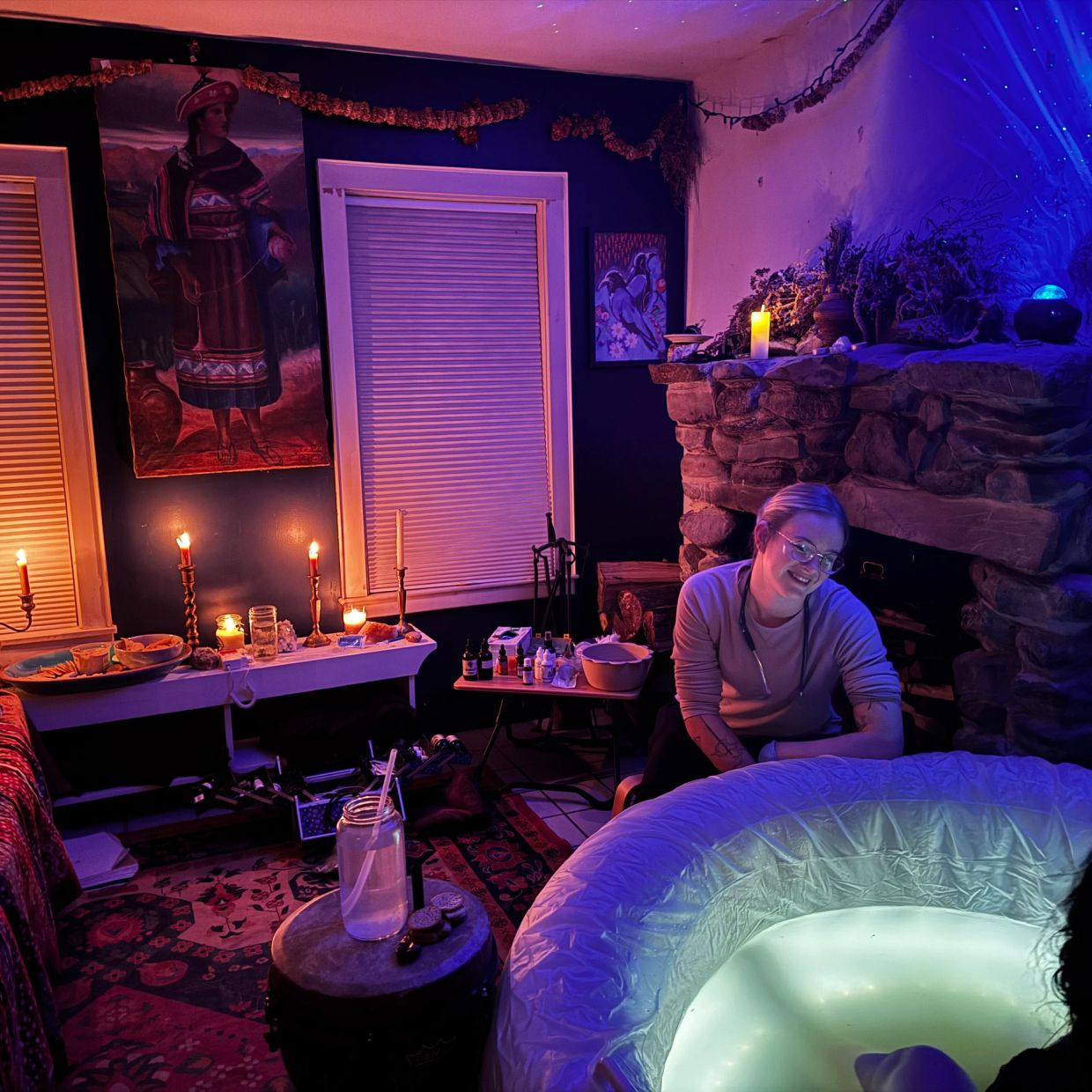 Woman smiling near an illuminated birthing pool in a cozy room.