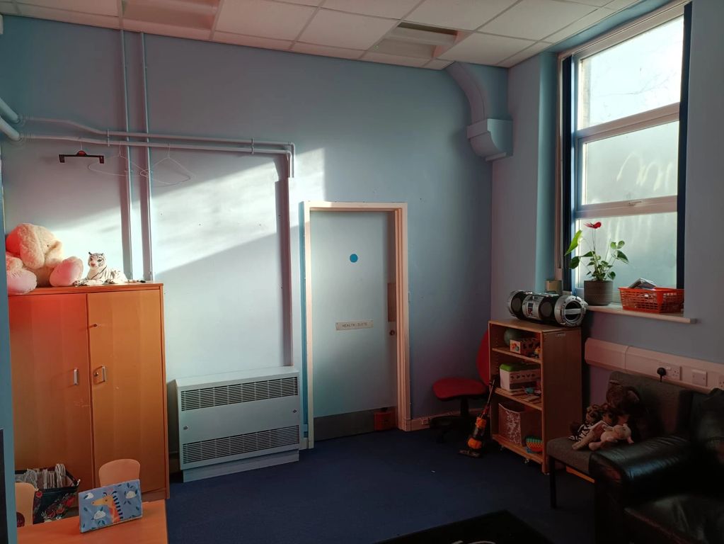 A small room, painted light blue with a cupboard, a bookshelf and a window on the right hand wall