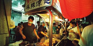 A man cooking street food in a stall with customers around him looking at the food he is preparing