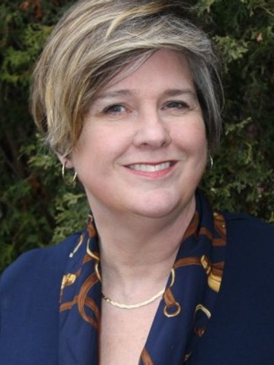 Smiling woman with short hair in a navy scarf and dark top.