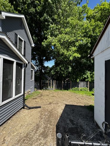 Backyard between two houses with trees and clear sky.