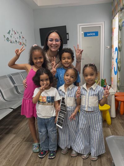 Niños sonriendo y mostrando señales de paz con una mujer.
