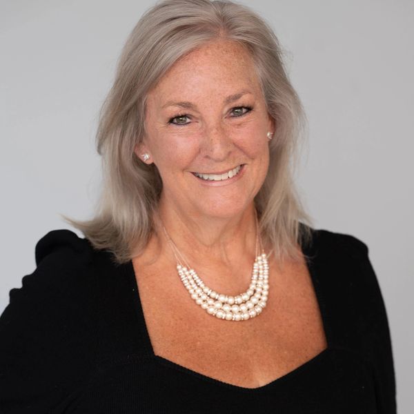 Smiling woman with gray hair wearing a black top and pearl necklace.