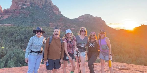 Group of six friends hiking on red rocks at sunset in a mountainous area.