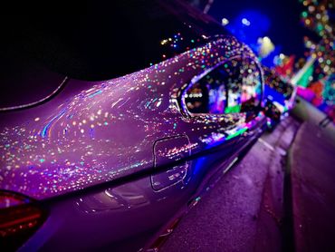 Reflections of colorful lights on a purple car at night.