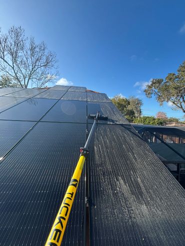 Cleaning solar panels with a long pole under clear blue sky.