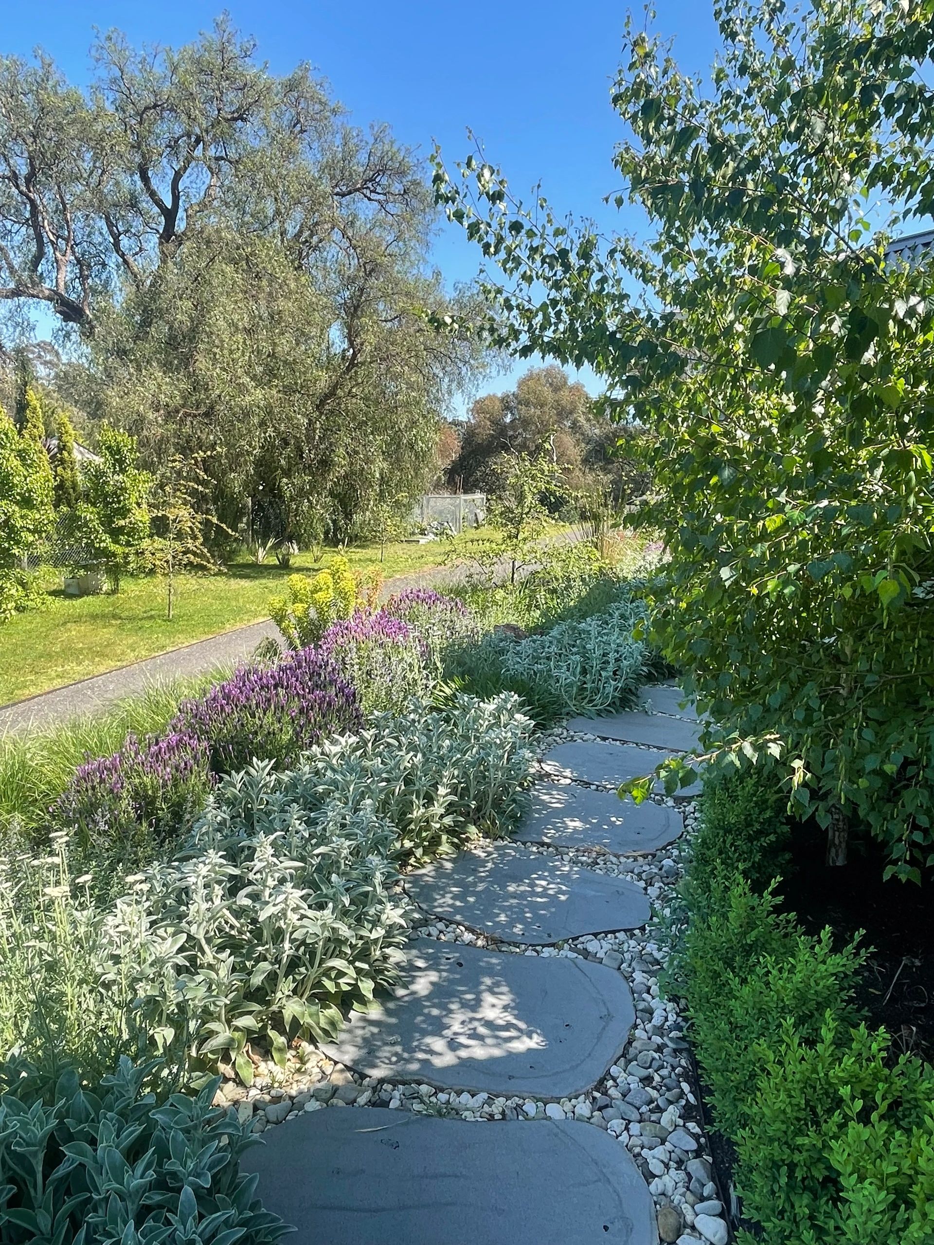 A serene garden path surrounded by lush greenery and flowers under a clear blue sky.