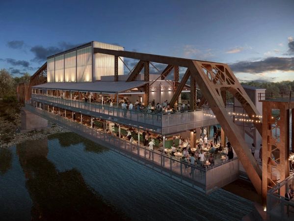 A vibrant restaurant built on a rusty iron bridge over water during sunset.
