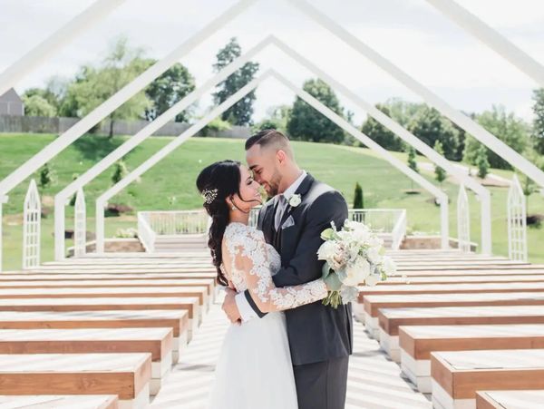 Newlyweds embrace in an outdoor wedding venue with wooden benches and white arch frames.