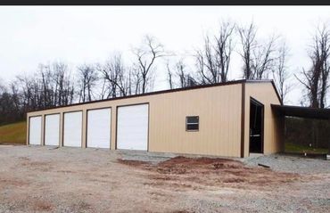 A beige metal building with five white garage doors in a rural area.