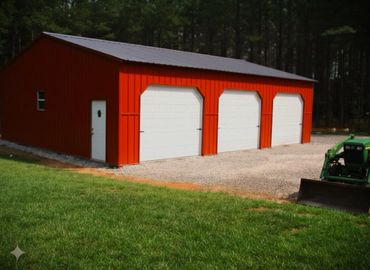 Red metal garage with three white doors and a green tractor parked nearby.