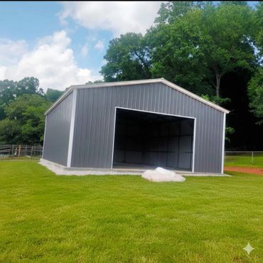 A gray metal storage building on a grassy lawn with trees in the background.