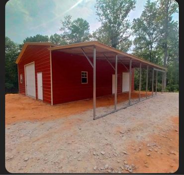 New red barn with metal roof and side extension in a forest clearing.